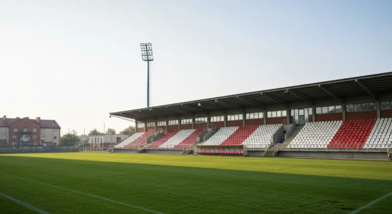 Pusty miejski stadion pilkarski w Radomiu o poranku - zielona murawa, biało-czerwone trybuny i maszty oswietleniowe w na